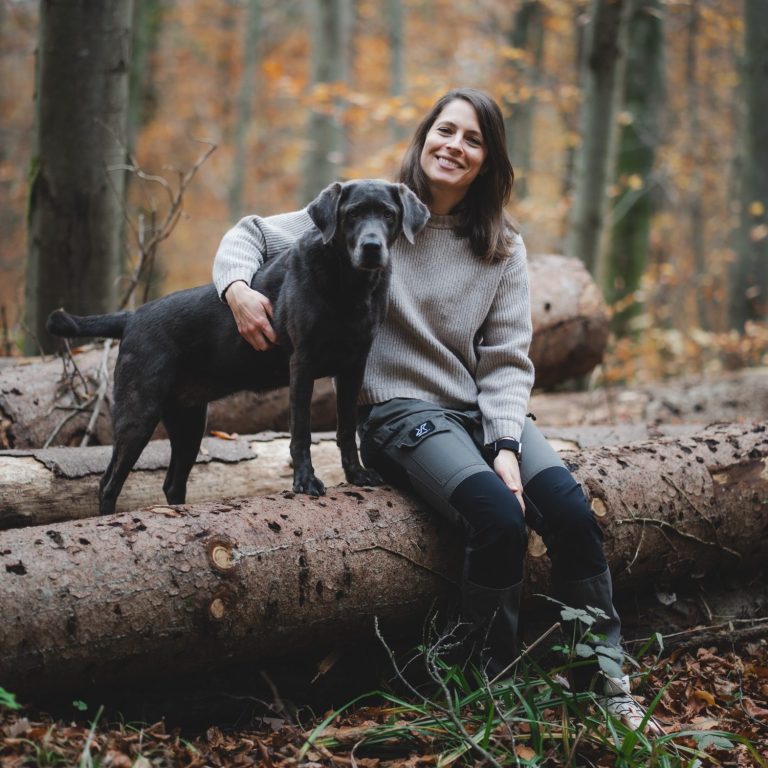 Hund & Trainerin auf einem Baumstamm